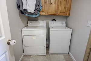 Laundry room featuring cabinet space, baseboards, washer and clothes dryer, and light wood-style flooring