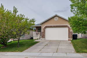 Single story home featuring driveway, a garage, brick siding, a front lawn, and stucco siding