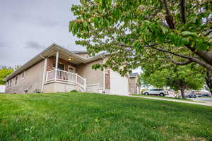 View of side of property with covered porch, a lawn, an attached garage, and stucco siding