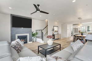 Living area featuring ceiling fan, light wood finished floors, a glass covered fireplace, recessed lighting, and stairway