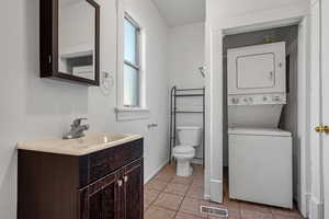 Bathroom with vanity, toilet, tile patterned floors, stacked washer / dryer, and visible vents