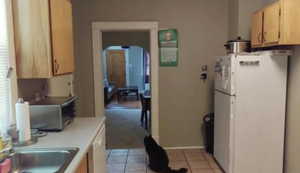 Kitchen with light countertops, arched walkways, freestanding refrigerator, stainless steel microwave, and light tile patterned floors