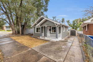 Bungalow-style home featuring an outdoor structure, fence, covered porch, a storage unit, and concrete driveway