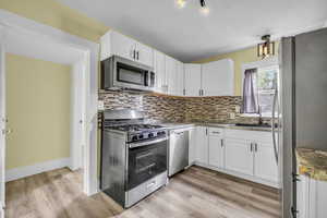 Kitchen featuring white cabinets, appliances with stainless steel finishes, a sink, light wood finished floors, and tasteful backsplash