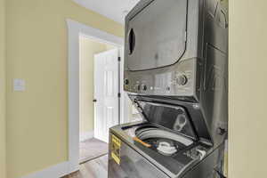 Washroom with baseboards, stacked washer / drying machine, wood finished floors, and laundry area