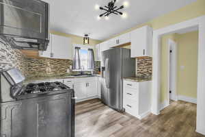 Kitchen featuring white cabinets, stainless steel fridge with ice dispenser, a sink, backsplash, and range with gas cooktop