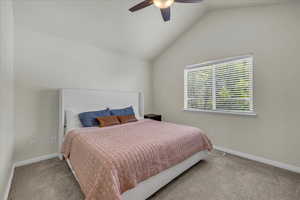 Carpeted bedroom featuring a ceiling fan, baseboards, visible vents, and lofted ceiling