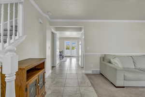 Living room with crown molding, baseboards, stone tile flooring, and visible vents