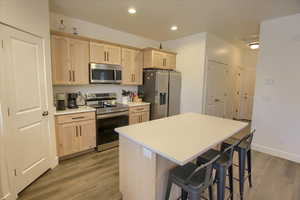 Kitchen with appliances with stainless steel finishes, a kitchen bar, light wood finished floors, and light brown cabinets
