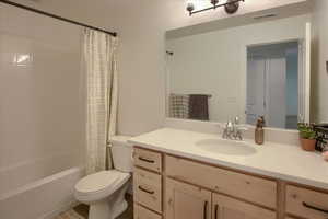 Bathroom with vanity, shower / bath combo, toilet, and visible vents