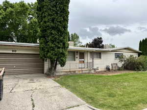 Ranch-style house with an attached garage, brick siding, a front yard, concrete driveway, and covered porch
