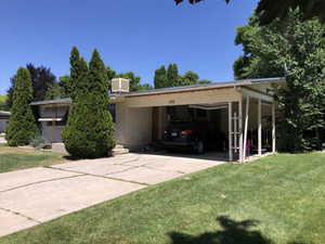 View of front of home featuring a front yard, cooling unit, brick siding, driveway, and a carport