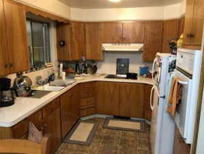 Kitchen with light countertops, under cabinet range hood, brown cabinets, and white appliances