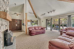 Carpeted living room featuring ceiling fan, a fireplace, track lighting, high vaulted ceiling, and beamed ceiling