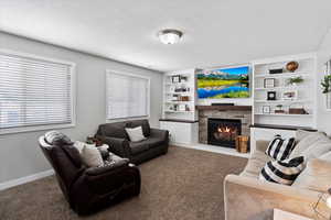Living area featuring a stone fireplace, built in bookcases, lots of natural light, and carpet flooring