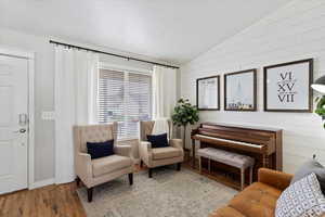 Sitting room featuring wood LVP flooring, wooden walls, shiplap, and vaulted ceiling