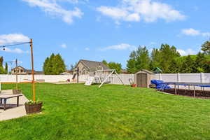 View of yard featuring a trampoline, an outdoor structure, a playground, a fenced backyard, and a storage unit