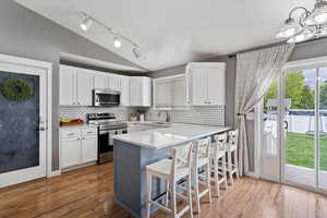 Kitchen featuring white cabinets, stainless steel appliances, quartz countertops, and lofted ceiling