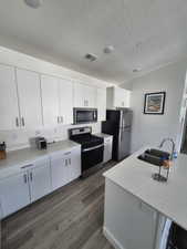 Kitchen with a sink, dark wood finished floors, stainless steel appliances, white cabinetry, and visible vents