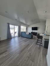 Living room with a textured ceiling, vaulted ceiling, wood finished floors, and visible vents