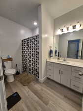 Bathroom featuring vanity, wood finished floors, toilet, baseboards, and a tile shower