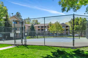 View of tennis court with a gate, fence, and a yard