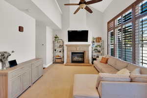 Living room with plenty of natural light, a glass covered fireplace, ceiling fan, and light colored carpet