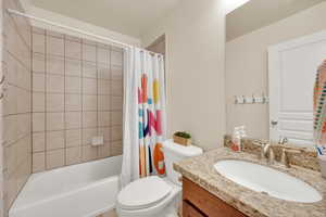 Full bathroom with toilet, shower / bathtub combination with curtain, and vanity