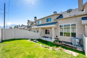 Back of property with fence, stucco siding, a chimney, cooling unit, and a lawn