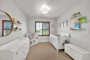 Bedroom featuring a nursery area, baseboards, light carpet, and visible vents