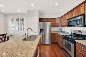 Kitchen featuring light stone countertops, a sink, stainless steel appliances, recessed lighting, and dark wood-style floors