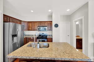 Kitchen with a sink, light stone counters, stainless steel appliances, recessed lighting, and an island with sink