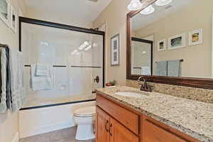 Full bath featuring tile patterned flooring, visible vents, vanity, toilet, and shower / bath combination with glass door