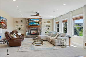 Carpeted living area with built in features, a fireplace, baseboards, recessed lighting, and a ceiling fan
