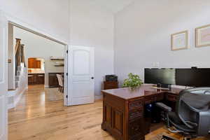 Office area featuring arched walkways, light wood finished floors, and high vaulted ceiling