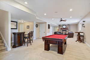 Recreation room with light carpet, baseboards, a stone fireplace, ceiling fan, and billiards