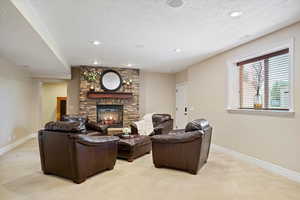 Living room with baseboards, a textured ceiling, a stone fireplace, and light colored carpet