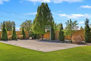 View of basketball court featuring a lawn, fence, and basketball hoop