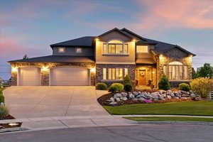 View of front facade with stone siding, driveway, stucco siding, a lawn, and an attached garage