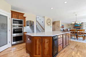Kitchen with stainless steel double oven, light wood-style flooring, built in microwave, and a kitchen island with sink