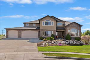 View of front of property with a front yard, stone siding, stucco siding, an attached garage, and driveway