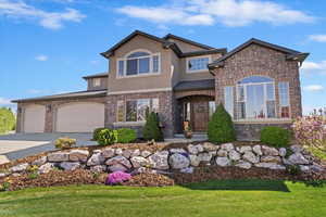 View of front of house featuring stucco siding, concrete driveway, a front lawn, and stone siding