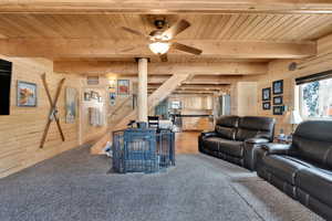 Living room with wood ceiling, light colored carpet, wood walls, beam ceiling, and stairs