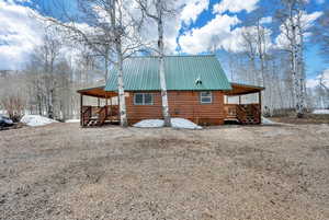 Rear view of house featuring covered porch, faux log siding, and metal roof