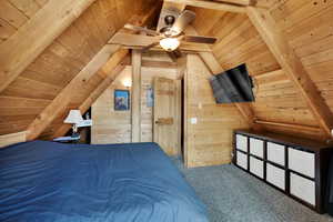 Carpeted bedroom featuring wooden walls, wooden ceiling, and vaulted ceiling with beams