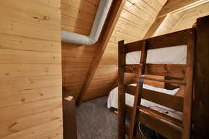 Unfurnished bedroom with wooden ceiling, carpet floors, vaulted ceiling, and wood walls