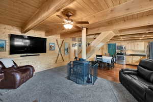 Living room with wooden walls, a ceiling fan, wooden ceiling, and beam ceiling
