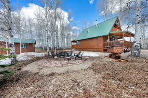 Rear view of property featuring metal roof, a wooden deck, faux log siding, an outdoor structure, and a fire pit