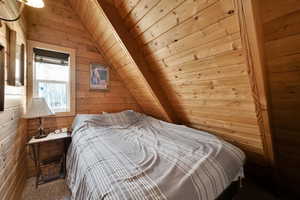 Carpeted bedroom with wooden walls, vaulted ceiling, and wood ceiling