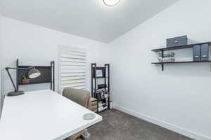 Office area featuring vaulted ceiling, dark colored carpet, and baseboards